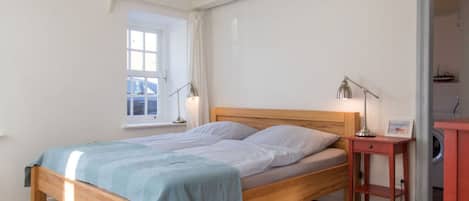 A bedroom with a wooden bed, two bedside lamps, a small wooden nightstand, and a window with curtains.