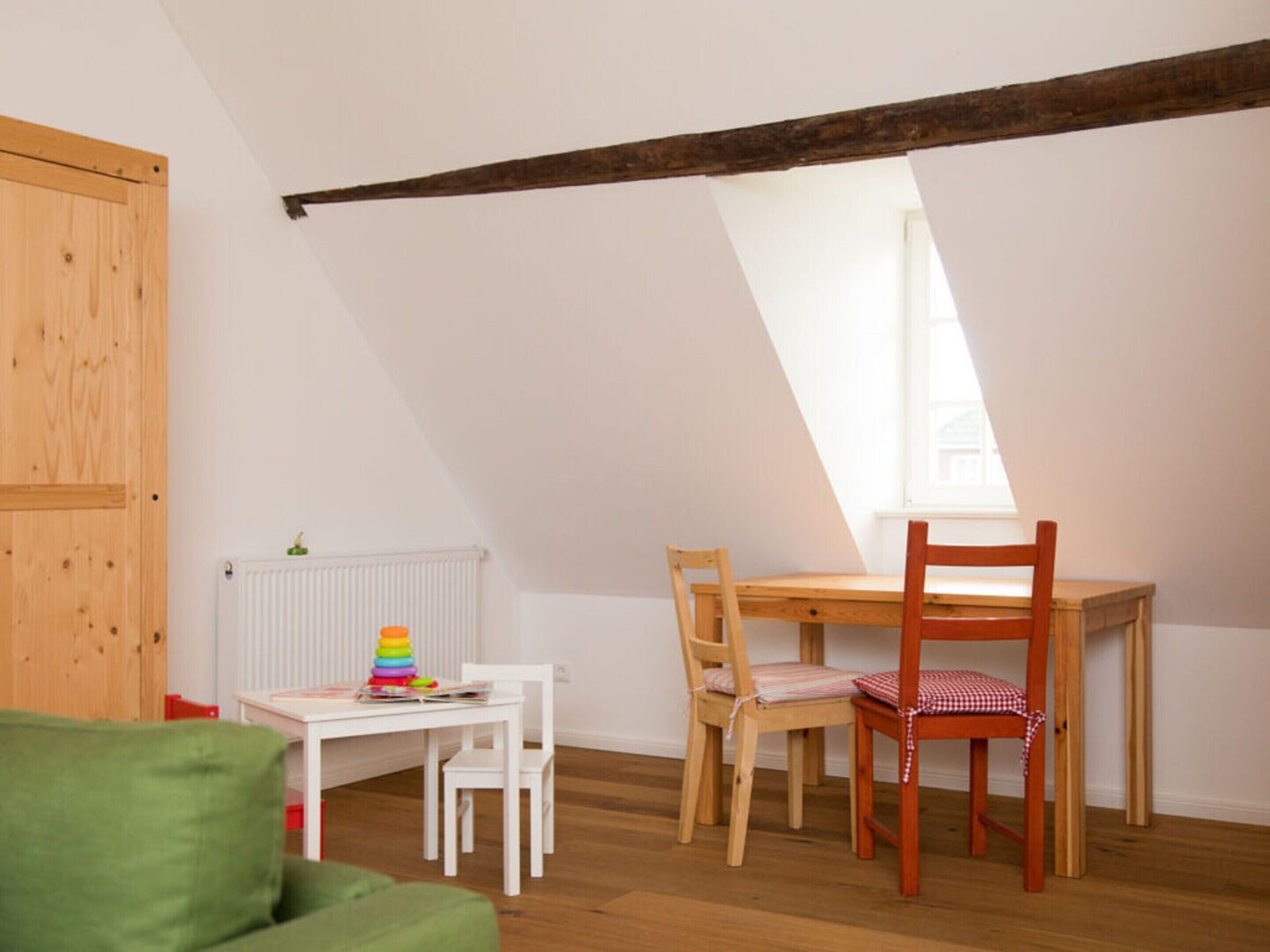 A room with a sloped ceiling, a wooden door, a radiator, a white table with chairs, and a window.