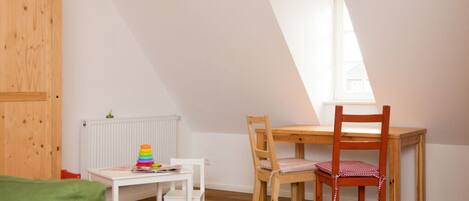 A room with a sloped ceiling, a wooden door, a radiator, a white table with chairs, and a window.