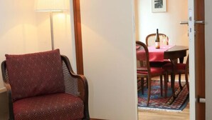 A room with a patterned armchair, a lamp, a dining table with chairs, and a door leading to another room. - Apartment Pinot Noir (Lorch)
