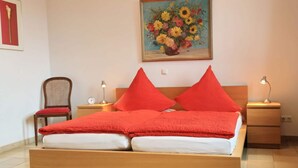 A neatly made bed with red bedding, a wooden headboard, and two bedside lamps. - Apartment Pinot Noir (Lorch)
