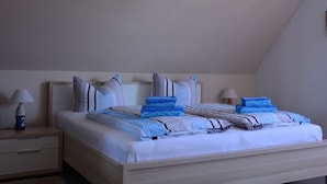 Una cama bien hecha con ropa de cama azul y blanca, un cabecero de madera y una mesita de noche con una lámpara.