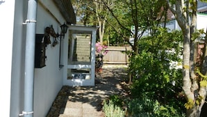 Un sendero estrecho que conduce a una puerta blanca con un ventanal pequeño, rodeado de follaje y una cerca de madera.