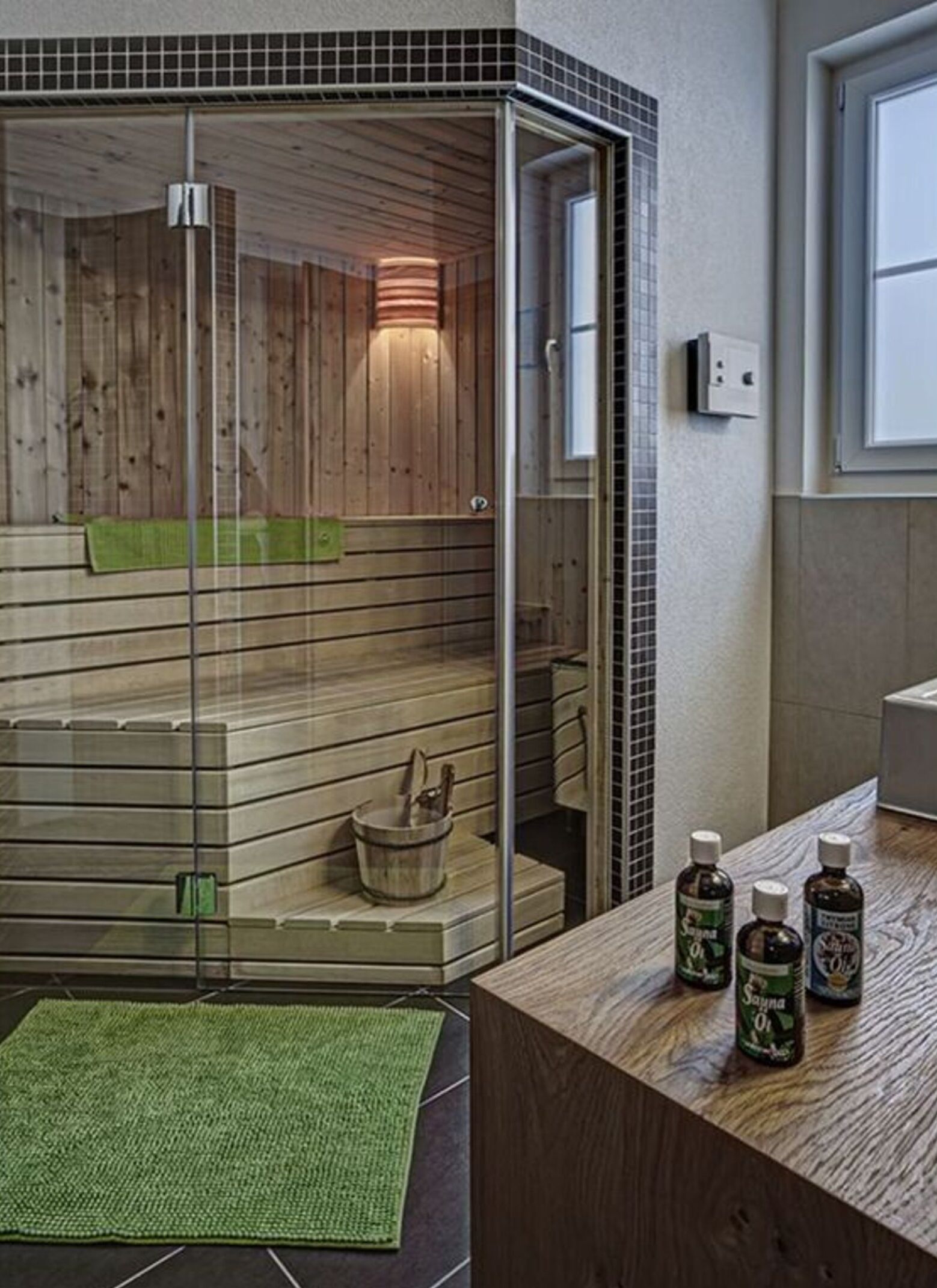 A modern bathroom with a glass-enclosed sauna, wooden benches, and a green mat.