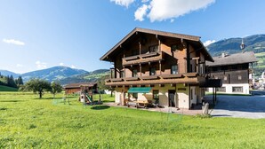 A traditional wooden chalet with a balcony, surrounded by a green field and mountains in the background. - Beautiful Apartment With Stunning View (Mittersill)