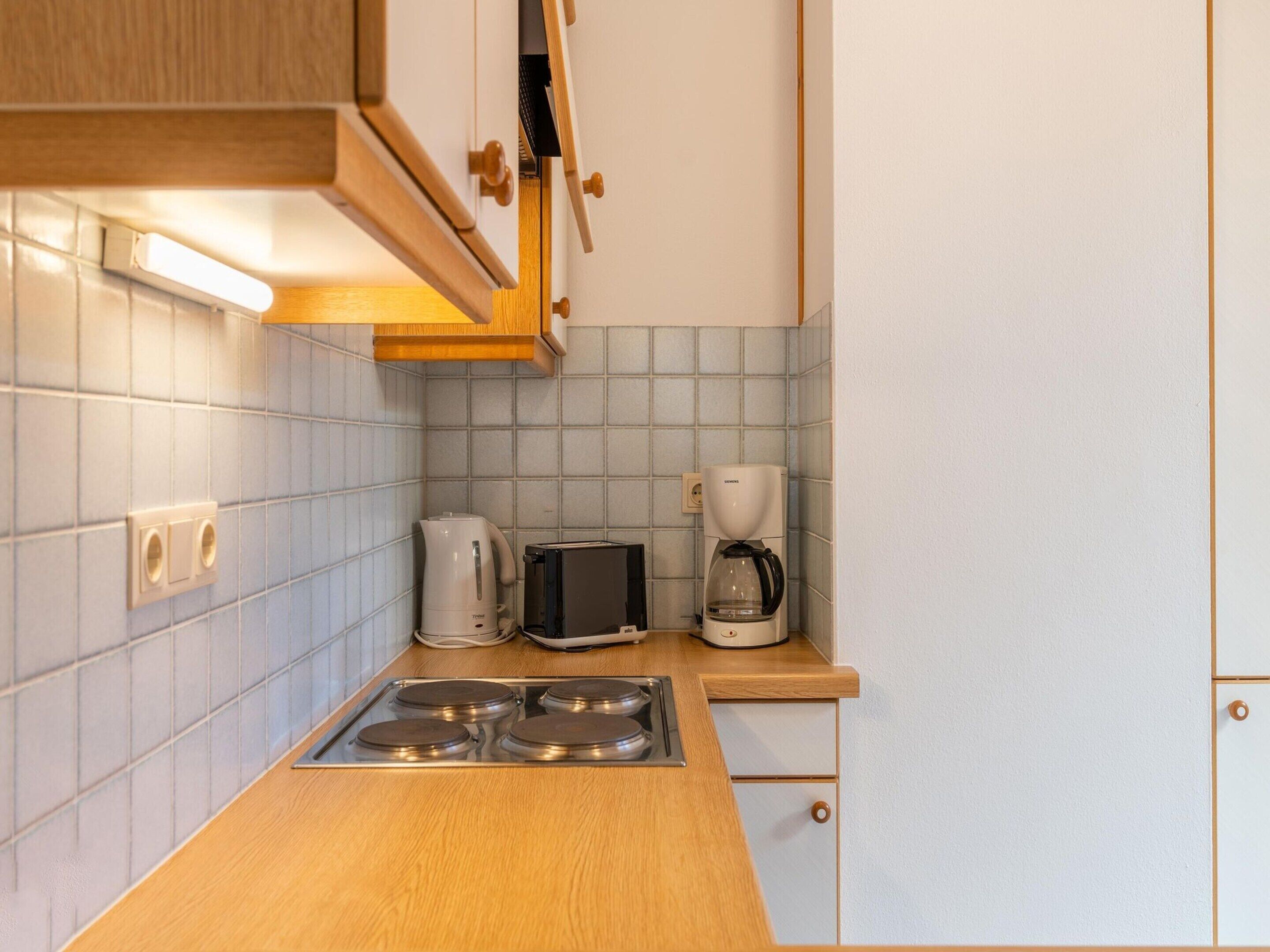Een kleine keuken met een houten aanrecht, een broodrooster, een koffiezetapparaat en een fornuis.