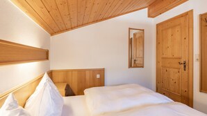 A bedroom with a wooden ceiling, a large wooden door, and a bed with white bedding. - Beautiful Apartment With Stunning View (Mittersill)