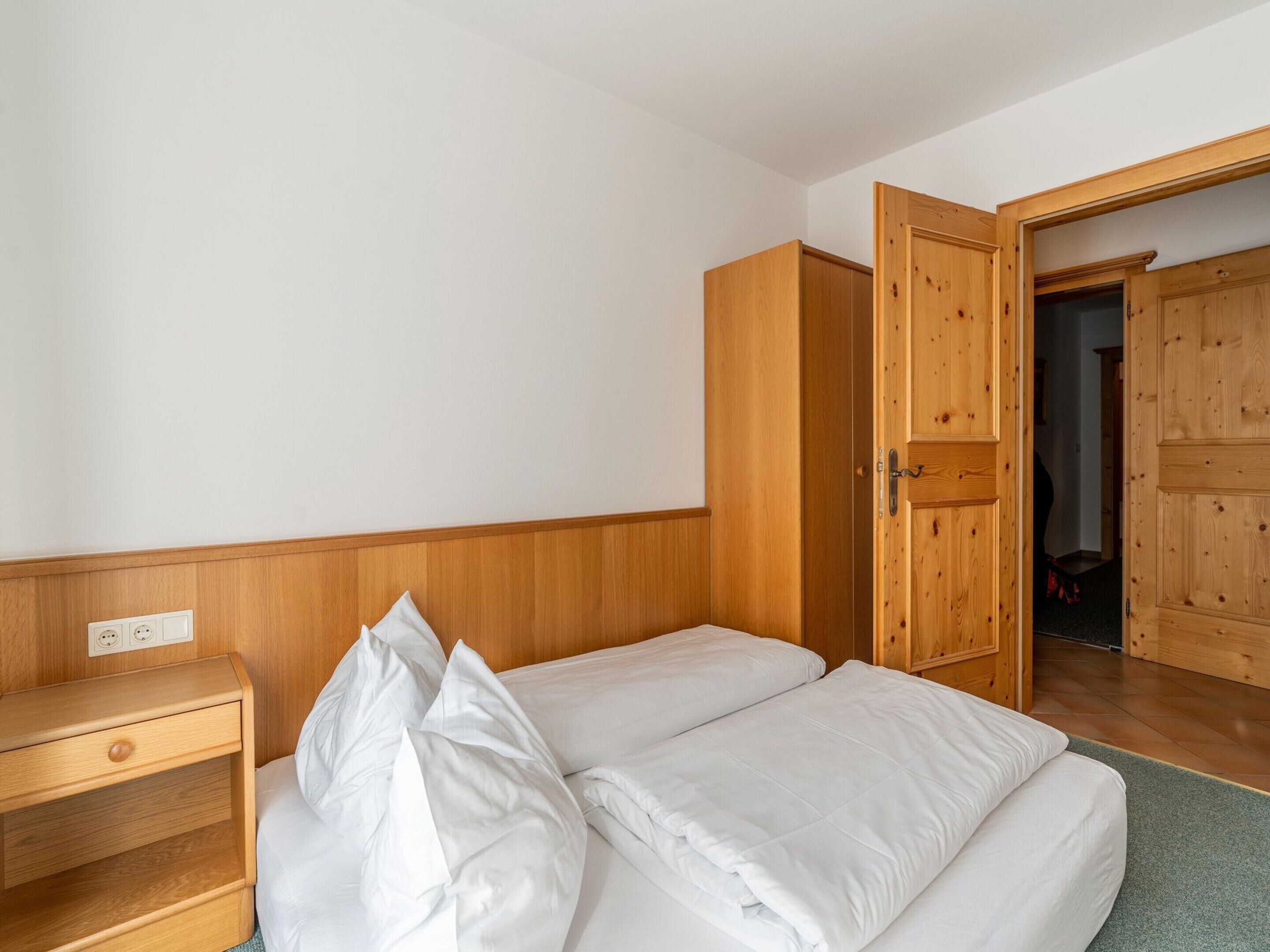 A bedroom with a bed, a wooden wardrobe, and a small bedside table.
