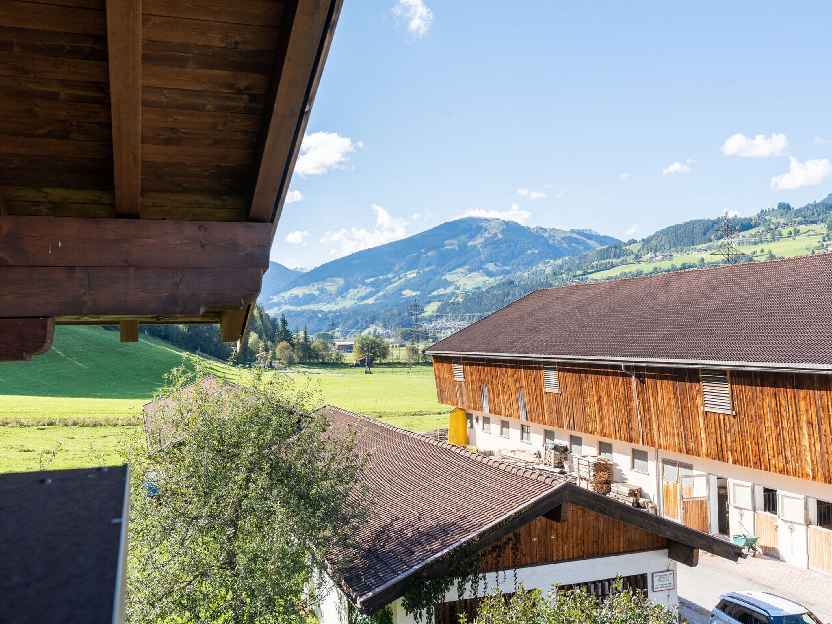 Un bâtiment en bois, doté d’un toit en pente, entouré de champs verdoyants et avec des montagnes en arrière-plan.