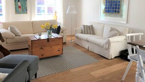 A modern living room with two white sofas, a wooden coffee table with flowers, a patterned rug, and artwork on the walls. - Holiday Home Scheersbergkate (Steinbergkirche)