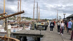 A wooden pier with a docked boat, a wooden walkway, and a view of the marina with several boats and buildings in the background. - Holiday Home Scheersbergkate (Steinbergkirche)