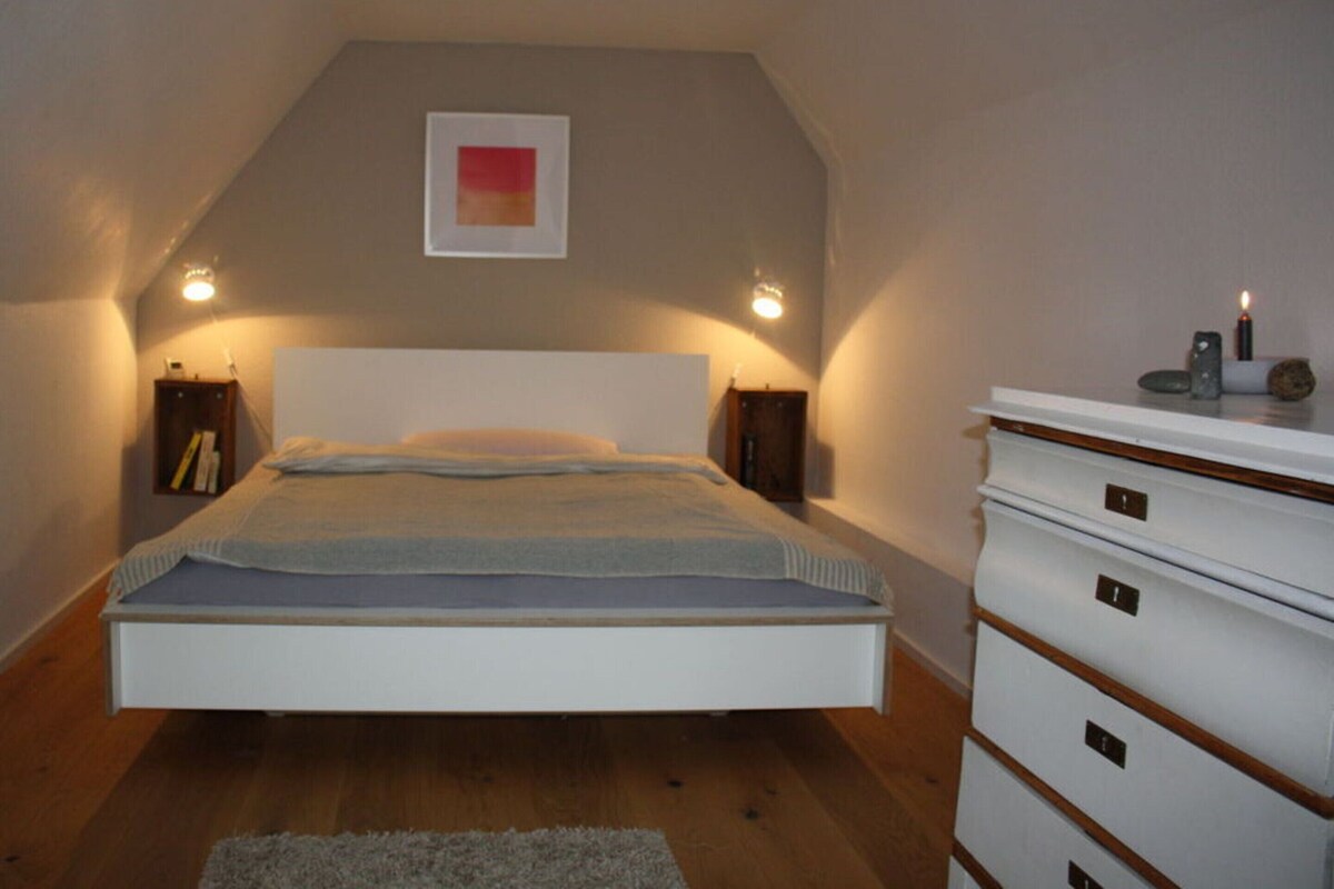 Um quarto com cama, mesas de cabeceira, cômoda e um quadro na parede.