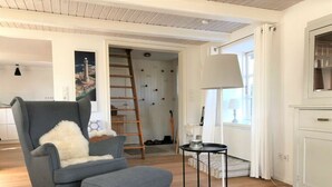 A modern living room with a grey armchair, a small ottoman, a round side table, and a white cabinet. - Holiday Home Scheersbergkate (Steinbergkirche)