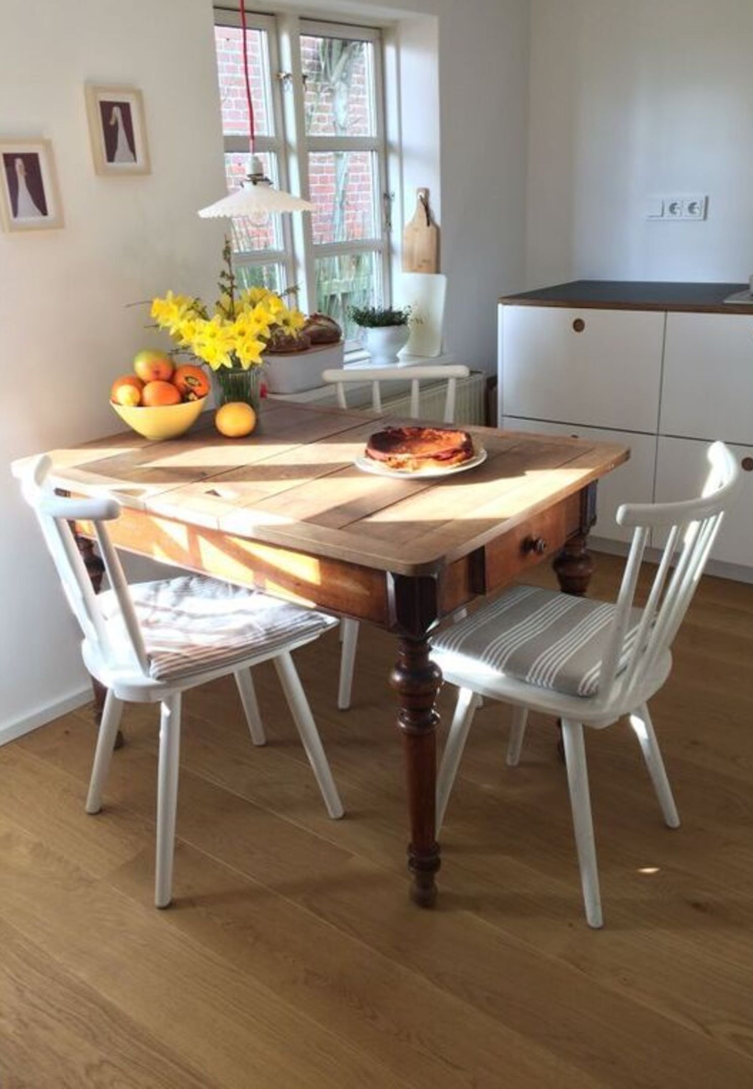 Ein Essbereich mit einem Holztisch, weißen Stühlen, einer Obstschale und einem Blumenstrauß.