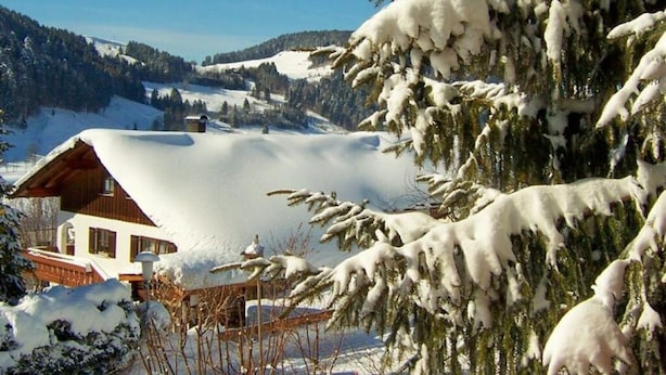 A snow-covered cabin with a wooden exterior, surrounded by snow-laden trees and a mountainous backdrop. - Kreuzwiesen Comfortable Holiday Residence (Missen-Wilhams)
