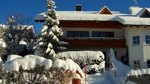 A two-story building with a snow-covered roof and a visible chimney. - Kreuzwiesen Comfortable Holiday Residence (Missen-Wilhams)