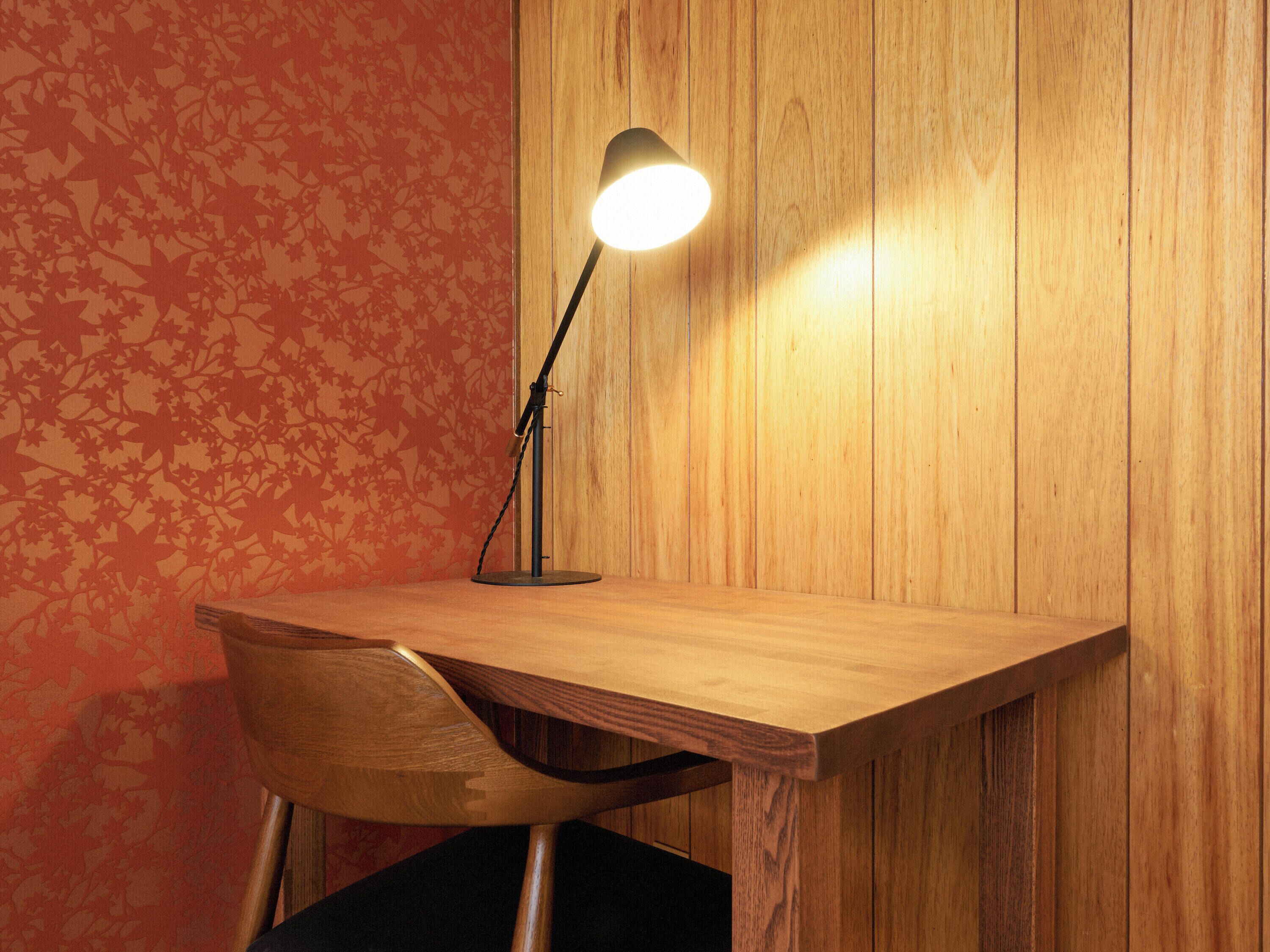 A wooden desk with a lamp, a chair, and a patterned wall.