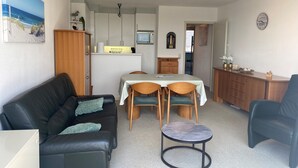Un espacio habitable compacto con sofá, una mesita redonda, una mesa de comedor con sillas, una kitchenette y un reloj en la pared.