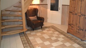 A staircase with wooden steps leading to a landing, a brown leather armchair with a cushion, a white door with a glass panel, and a wooden cabinet. - Saupe Comfortable Holiday Residence (Schaprode)