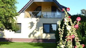 A two-story house with a balcony, a clear sky, and a garden with flowers. - Saupe Comfortable Holiday Residence (Schaprode)