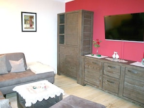A living room with a grey sofa, a wooden cabinet, a television, and a small table with a vase and figurines. - Saupe Comfortable Holiday Residence (Schaprode)