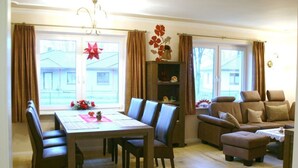 A living room with a dining table, chairs, a sofa, and a window with curtains. - Saupe Comfortable Holiday Residence (Schaprode)