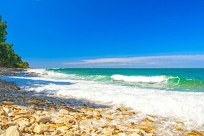 Ein felsiger Strand mit klarem, blauem Wasser und einer Baumreihe.