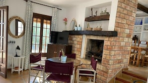 Een gezellige woonkamer met een open haard, een televisie en een eethoek met stoelen en een tafel.