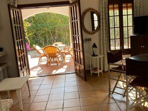 An open doorway leading to a patio with a table and chairs, a small round table with a lamp, and a television on a stand. - Spacious Holiday Home With Private Garden (Carboneras)