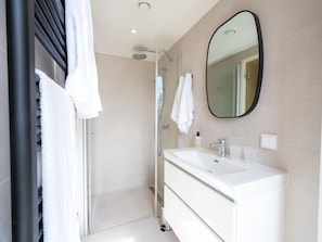A modern bathroom with a glass shower enclosure, a white vanity with a mirror, and a towel rack.