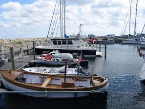 A marina with several boats docked, including a small wooden boat with a cabin and a larger white boat with a flag. - 2 Person Holiday Home in Albaek (Aalbaek)