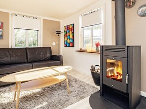 A living room with a black sofa, a wooden coffee table, a black wood-burning stove, and a colorful wall art piece. - 2 Person Holiday Home in Albaek (Aalbaek)