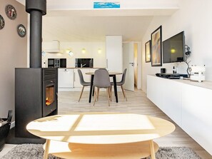 A modern kitchen with a central island, a dining area with chairs, a black wood-burning stove, and a flat-screen TV mounted on the wall. - 2 Person Holiday Home in Albaek (Aalbaek)