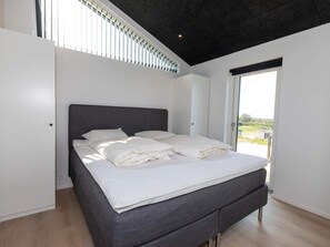 A modern bedroom with a large bed, a dark ceiling, and a view through a window.
