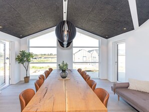 A spacious dining area with a long wooden table, multiple chairs, a potted plant, and a modern pendant light.