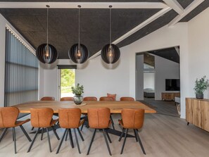 A modern dining area with a long wooden table, six brown chairs, and three hanging pendant lights. - 4 Star Holiday Home in Saltum (Saltum)