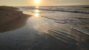 Ein Strand bei Sonnenuntergang, ruhige Wellen und Fußspuren im Sand.