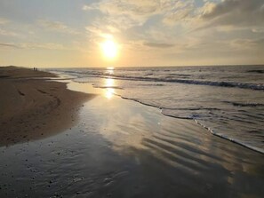 Une plage au coucher du soleil, avec des vagues calmes et des empreintes de pas dans le sable.