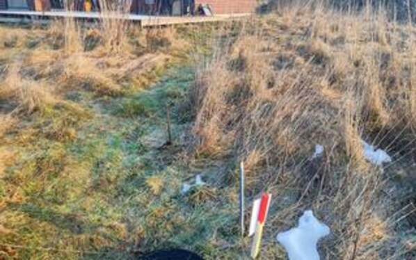 A grassy outdoor area with a red and white sign, possibly a trail marker or informational sign.