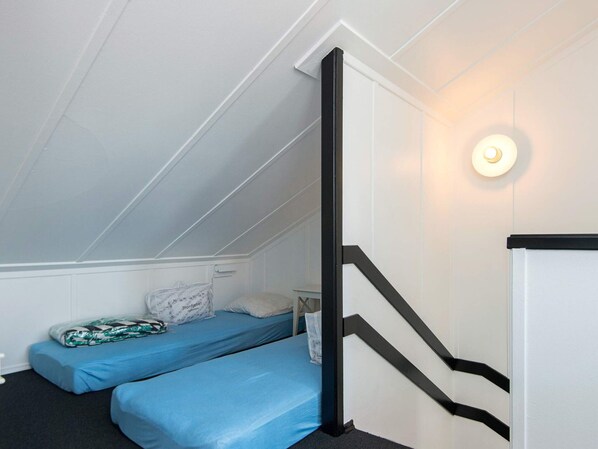 Habitación tipo dormitorio con dos camas individuales, una mesita y una escalera.