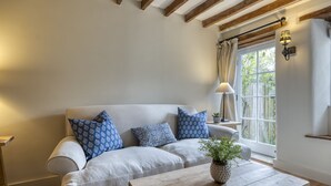 Uma sala de estar acolhedora com um sofá de cor clara, almofadas estampadas, uma mesa de centro de madeira e uma janela com cortinas.