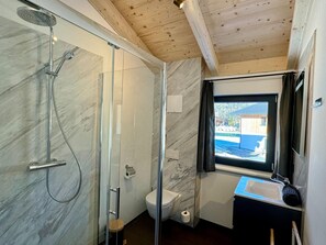 Ein modernes Badezimmer mit Duschkabine aus Glas, Toilette und Waschbecken mit Blick aus dem Fenster.