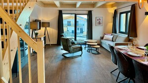 A modern interior with a wooden staircase, a sofa, a dining table set for two, and a view of the outside. - Chalet Near Lake Pressegger and Nassfeld ski Area (Hermagor-Pressegger See)
