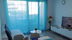 A room with a dining table, chairs, a sofa, a TV, and a window with curtains. - Apartment With Beach View (Benalmádena)