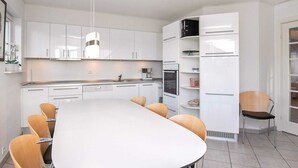 A modern kitchen with white cabinets, a large island with chairs, and built-in appliances. - 8 Person Holiday Home on a Holiday Park in Bogense (Bogense)