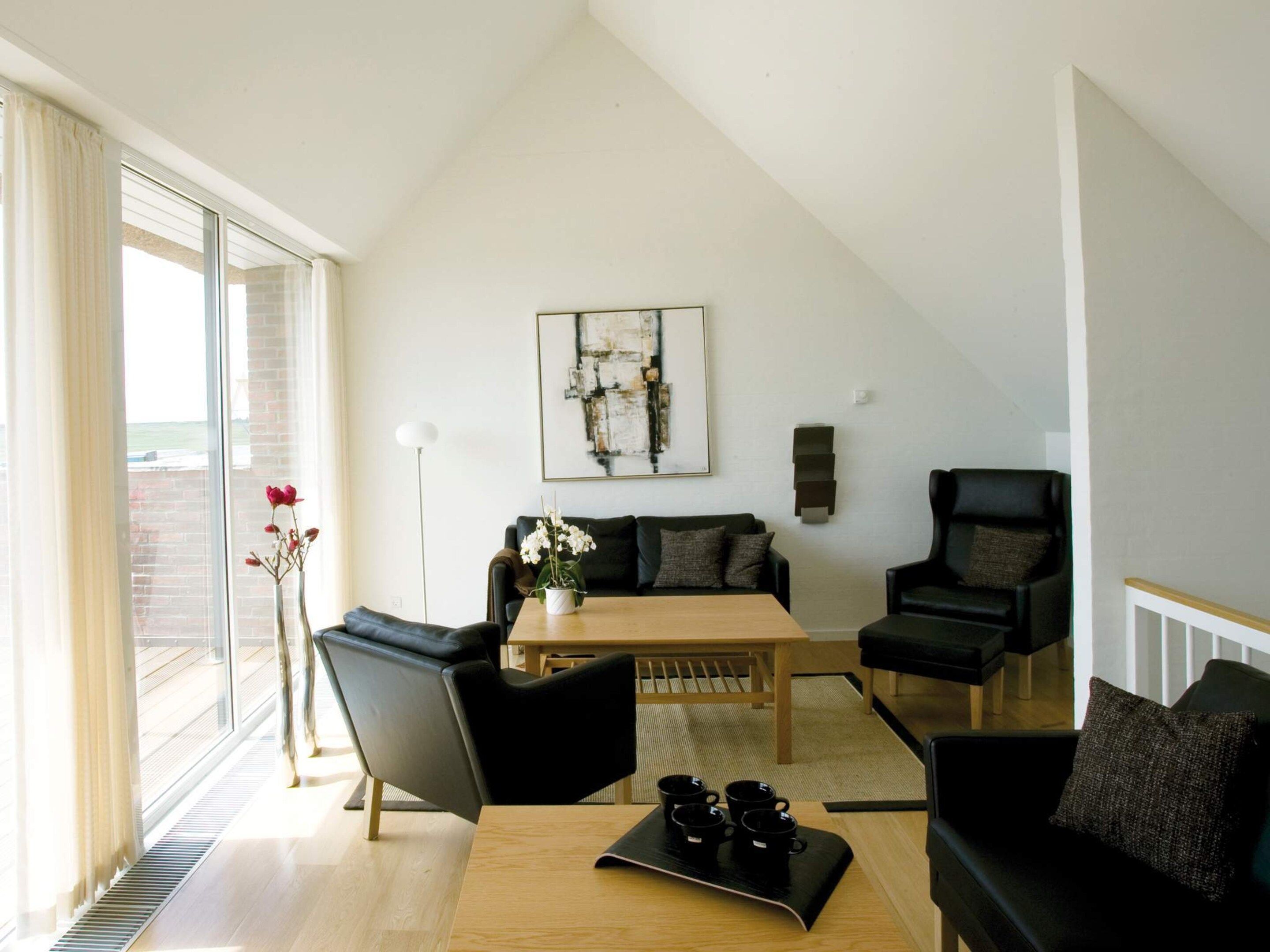 A modern living room with a high ceiling, a dining table with chairs, a sofa, and a coffee table with cups.