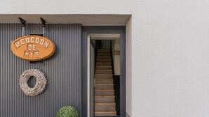 Une pancarte en bois avec du texte, une couronne et une plante en pot, placées à l’entrée d’un bâtiment.
