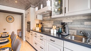 Une cuisine moderne avec des meubles blancs, un four encastré, une machine à café et un meuble vitré contenant des objets décoratifs.