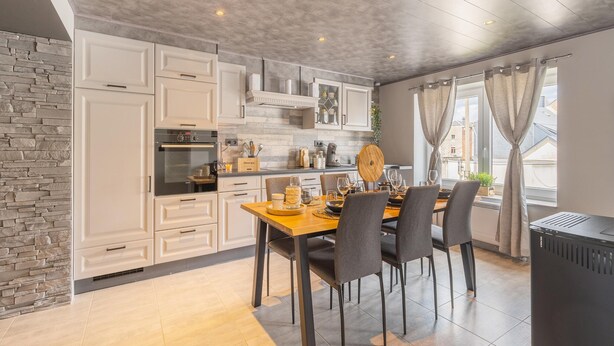 Une cuisine moderne avec des meubles blancs, un mur d’accent en pierre et un coin repas comprenant une table et des chaises en bois.