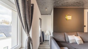 Un salon moderne avec un canapé gris, un luminaire fixé au mur et une vue sur des panneaux solaires à l’extérieur.